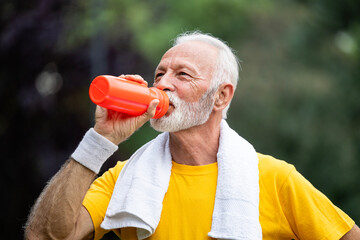 Close up view of active senior man drinking water after running.