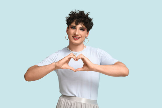Young transgender woman making heart gesture on blue background