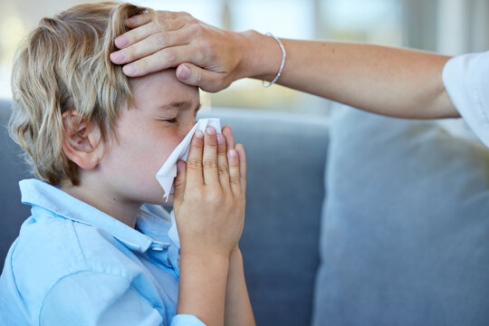 Blowing nose, child and hand of mother for fever with flu, cold or allergy on sofa at home. Sick, medical emergency and mom feel head of kid for high temperature with illness in living room at house.