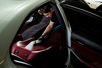 Hoovering car backseat with vacuum extractor. Detailing auto seats with special hoover nozzle.