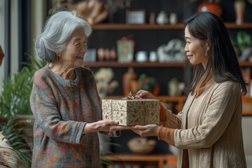 Elderly Asian woman receiving a gift from a young woman indoors. Concept of family, gratitude, and Christmas