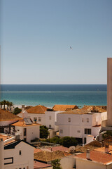 View from a Window in Portimão, Algarve, Portugal 2024. The image showcases traditional Portuguese rooftops with terracotta tiles, set against the backdrop of the beautiful blue Atlantic Ocean. July.