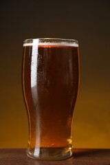 Glass with fresh beer on wooden table against dark background