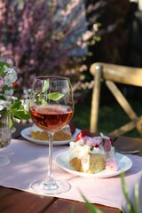 Vase with spring flowers, wine and cake on table served for romantic date in garden