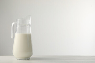 Glass jug with fresh milk on light wooden table. Space for text