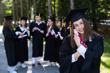 Group of happy students in graduation gowns outdoors. A young girl boasts of her diploma.