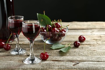 Bottle and glasses of delicious cherry liqueur with juicy berries on wooden table