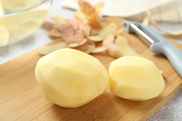 Fresh raw potatoes, peels and peeler on table, closeup
