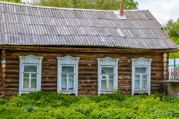 The facade of an abandoned wooden house with carved windows. The old residential architecture is destroyed and abandoned. A log wall with windows and a roof.