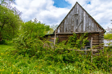 The facade of an abandoned wooden house with windows. The old residential architecture is destroyed and abandoned. A log wall with windows and a roof.
