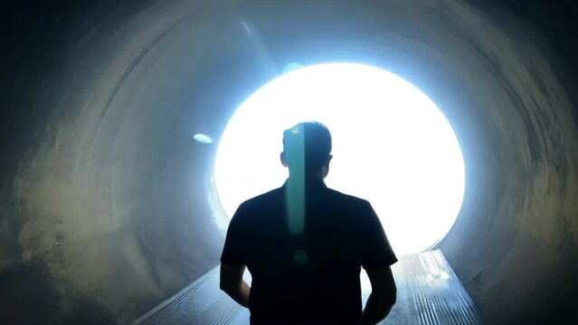 silhouette of man, shoulders slumped walking out of a dark tunnel towards a bright light