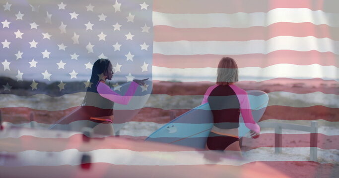 Image of flag of usa over happy diverse women with surfboards on beach in summer - Powered by Adobe
