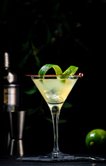 Classic alcoholic cocktail with vodka, syrup, lime, juice and ice in martini glass, dark background