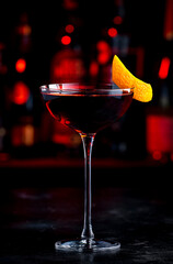Red cocktail drink with sherry, vermouth and orange zest, black bar counter background