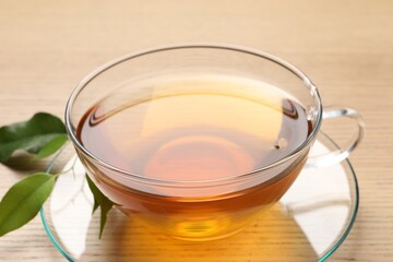 Refreshing green tea in cup and leaves on wooden table, closeup