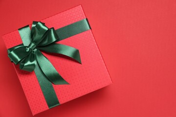 Gift box with green bow on red background, top view. Space for text