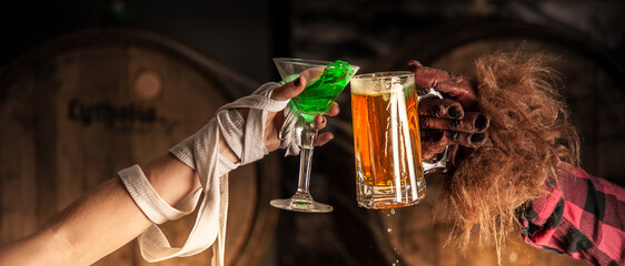 Hands of a person in a mummy costume and a person in a werewolf costume toasting with a green...