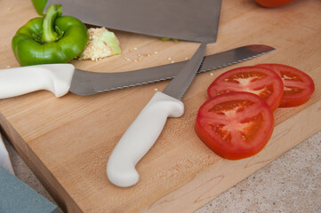 Sliced tomato, green bell pepper, and kitchen knives on a wooden cutting board