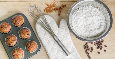 Baking ingredients and tools with muffins in a tray on a wooden surface