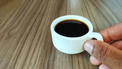  Hand holding cup of black coffee on the wooden table with copy space for design.
