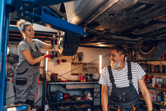 Smiling colleagues technicians standing at car repair shop and fixing car