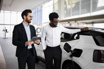 Dealer sells electric SUV to businessman at modern car dealership. Professional consultation with...