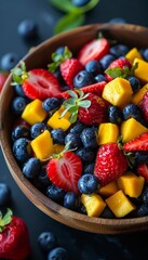 Fresh fruit salad with mango, strawberries and blueberries in a wooden bowl.
