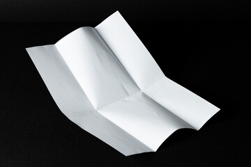 A blank white paper unfolds on a black background with copy space