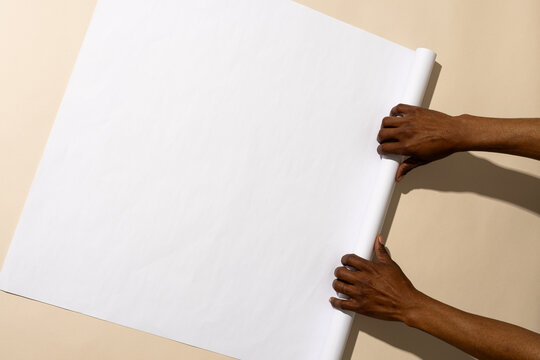 Hands unroll a blank white paper on a table, with copy space