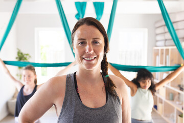 Portrait of happy diverse female coach, with teenage girls exercising at aerial yoga class