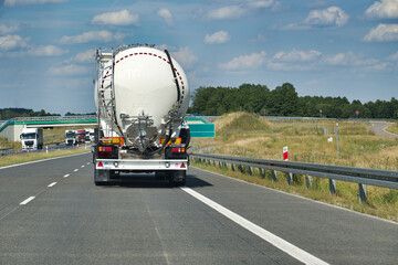 Cement tanker truck driving along highway in sunny countryside with other vehicles on the road