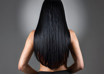 A woman with long black hair is standing in front of a grey background