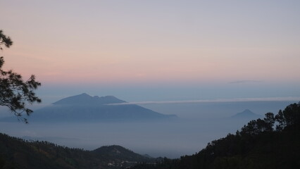 Aerial view of yellow sunrise over white puffy clouds with mountains on horizon. View on mountains and yellowy sky above clouds.