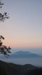 Aerial view of yellow sunrise over white puffy clouds with mountains on horizon. View on mountains and yellowy sky above clouds.