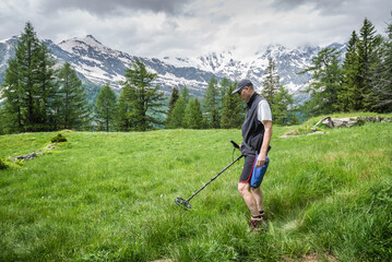 Man on a treasure hunt with a recreational metal detector in mountain meadows in summer with snow...