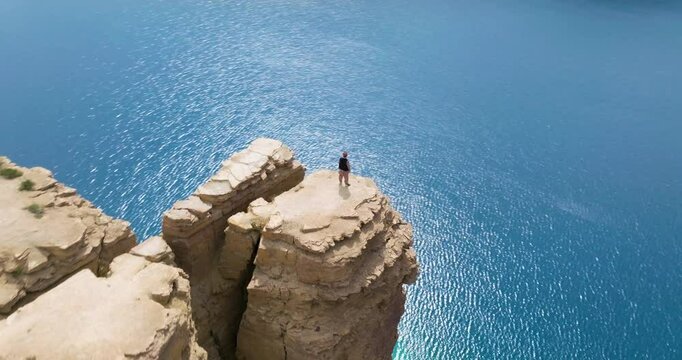 Male Hiker Stands On Clifftop With Scenic Lake View At Band-e Amir National Park In Afghanistan. aerial orbiting shot