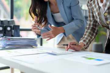 Two Asian businesswomen work together using laptops and documents to discuss planning analysis startup project. Customer contact and statistics, online markets, finance and investments at the office.