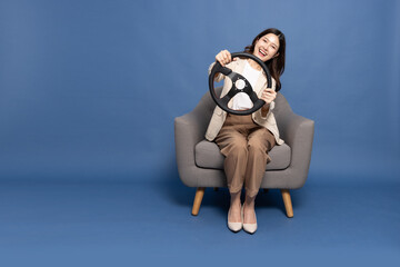 Young Asian businesswoman sitting on armchair and holding the steering wheel of a car isolated on...