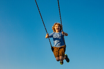 Kid on chain swing, having fun against blue sky. Carefree and freedom childhood. Active kid playing outdoors. Child at playground. Cute kid having fun on a playground outdoors in summer. Kid swinging.