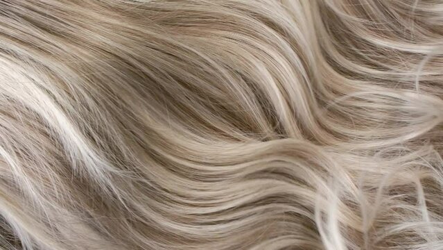 Close-up blond curly hair texture, female long hair background in slow motion