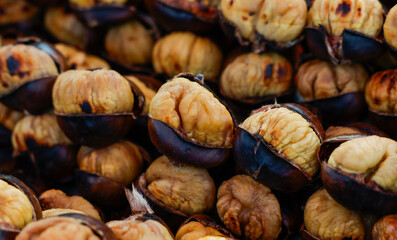 A close-up view of roasted chestnuts piled high at a market stall. The chestnuts are warm and inviting, with their shells slightly cracked open to reveal the soft, creamy interior.