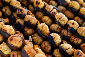 A close-up shot of roasted chestnuts, showcasing their brown, slightly burnt shells and light brown insides.