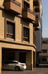 A tan apartment building with a white car parked in the garage. The building has multiple balconies with iron railings.