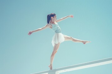 Obraz premium Elegant Ballerina Performing Balancing Act on a White Beam Against Clear Sky