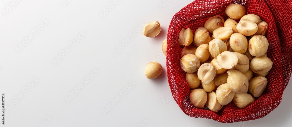 Poster Macadamia nuts are presented in a red mesh bag set against a white backdrop with copy space image.