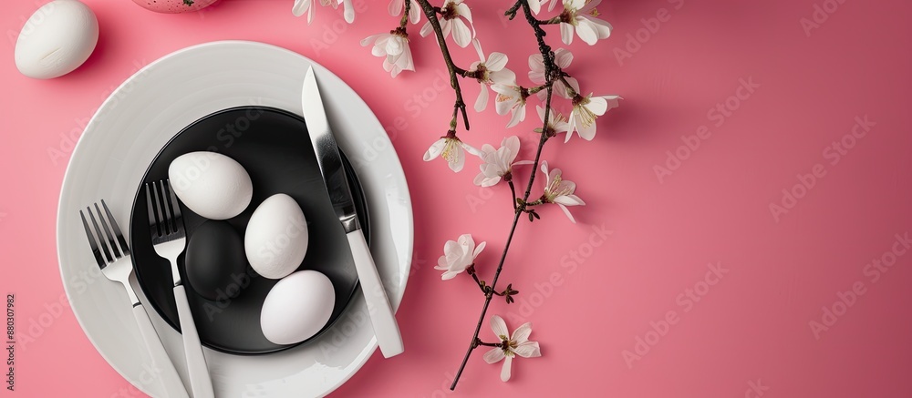 Poster top view of easter dinner setting featuring black and white eggs, knife, and fork on a pastel pink b
