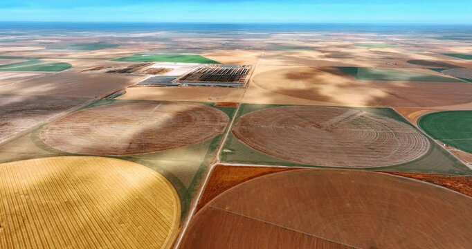 Flying above the farmlands with circle center-pivot-irrigation farms. Clouds shade the fields on sunny day.
