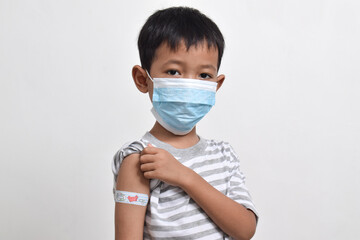 Asian boy using face mask with plaster bandage on his arm after vaccination. Vaccine injection. Child immunization. Health services for children. copy space
