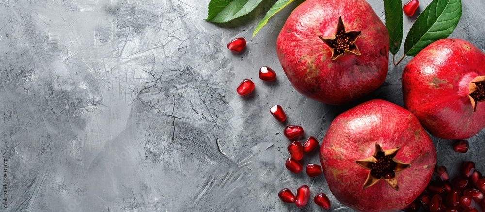 Poster a banner with copy space image featuring a ripe pomegranate fruit with green leaves against a grey c