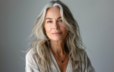 Naklejka premium A woman with long gray hair and a necklace is smiling. She is wearing a white shirt and she is happy
